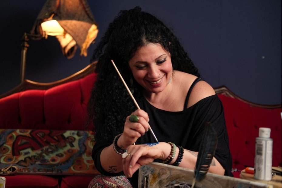 Filmmaker and artist Yaffa Goawily sits on a couch and paints on her hand.